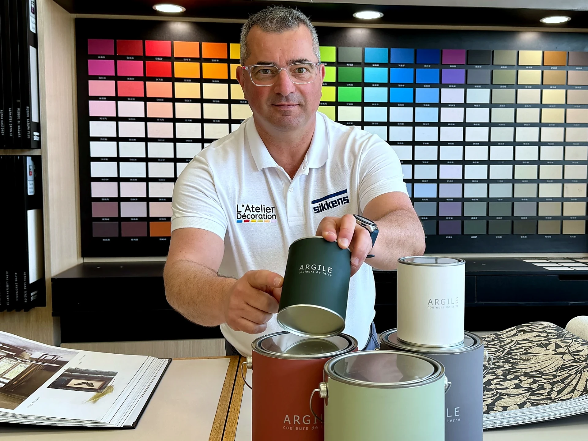 Conseiller L'Atelier Décoration présentant des pots Argile devant le grand nuancier de couleurs